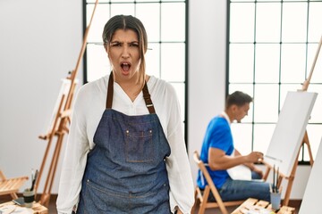 Young hispanic couple at art studio scared and amazed with open mouth for surprise, disbelief face