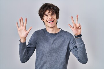 Young man standing over isolated background showing and pointing up with fingers number eight while smiling confident and happy.