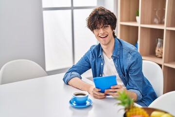 Young hispanic man driking coffee using touchpad at home