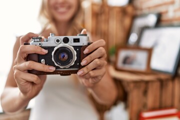 Young blonde woman smiling confident using vintage camera at home