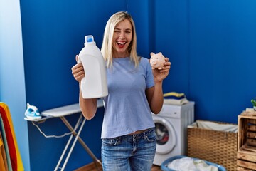 Beautiful woman doing laundry holding detergent bottle and piggy bank winking looking at the camera...