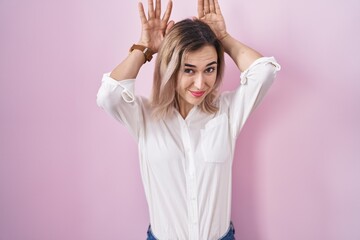 Young beautiful woman standing over pink background doing bunny ears gesture with hands palms...