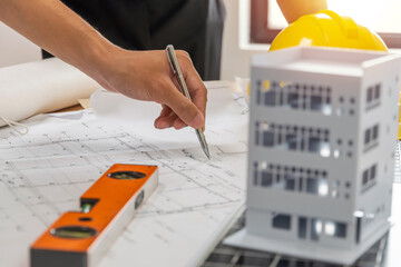 professional architect, engineer or interior hand reviewing blueprint with building model on workplace desk in office center at construction site, contractor, construction, engineering concept - obrazy, fototapety, plakaty