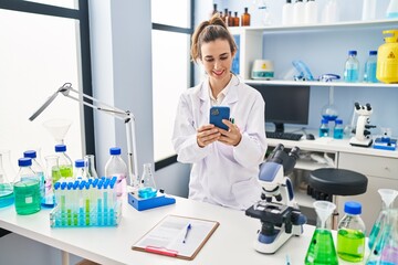 Fototapeta premium Young woman wearing scientist uniform using smartphone at laboratory