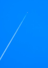 Jet airplane flying with white contrail on blue clear sky background in vertical frame