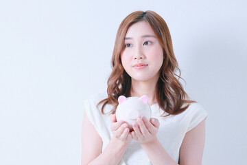 掌にブタの貯金箱を乗せ遠くを見つめる女性