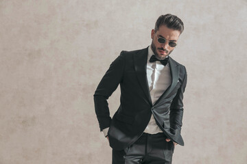 Fototapeta premium elegant fashion guy in black tuxedo with hands in pockets looking down