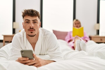 Young caucasian couple reading book and using smartphone at bedroom.