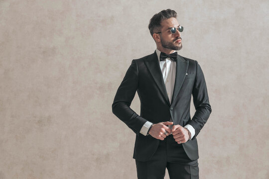 attractive elegant man looking to side while adjusting black tuxedo