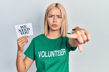Beautiful blonde woman wearing volunteer t shirt showing we need you banner pointing with finger to...