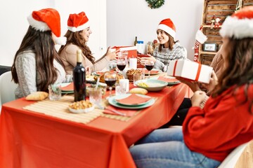 Group of young hispanic women having christmas dinner and giving gifts sitting on the table at home.