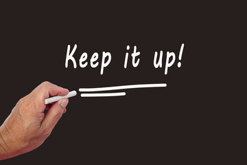 Male hand writes in white chalk pencil the word KEEP IT UP on a black background