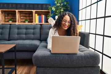 Young latin woman using laptop lying on sofa at home