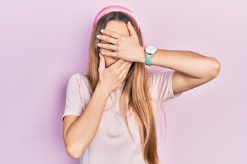 Young blonde girl wearing casual clothes covering eyes and mouth with hands, surprised and shocked. hiding emotion