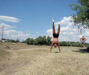 athletic man walking on his hands in nature in summer