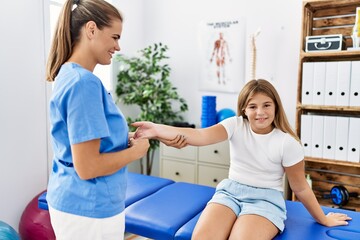 Fototapeta premium Woman and girl physiotherapist and patient having rehab session stretching hand at physiotherapy clinic