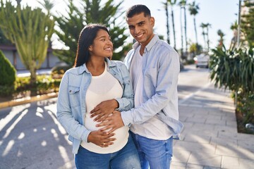 Young latin couple expecting baby touching belly at park