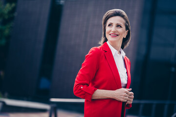 Photo of confident adorable mature lady wear red jacket walking enjoying good weather outdoors city...