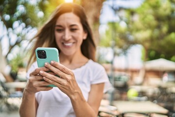 Young hispanic woman smiling confident using smartphone at park