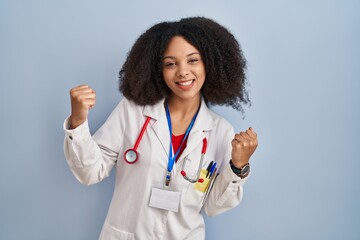 Young african american woman wearing doctor uniform and stethoscope very happy and excited doing winner gesture with arms raised, smiling and screaming for success. celebration concept.