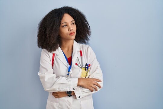 Young african american woman wearing doctor uniform and stethoscope looking to the side with arms crossed convinced and confident