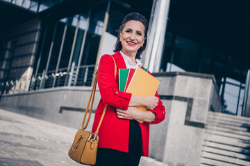 Photo of charming cheerful mature lady secretary wear red jacket holding documents folders outside...