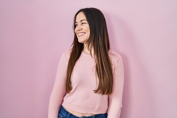 Obraz premium Young brunette woman standing over pink background looking away to side with smile on face, natural expression. laughing confident.