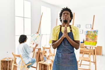 African young man standing at art studio begging and praying with hands together with hope...