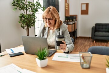 Middle age businesswoman smiling happy working and drinking coffee at the office.