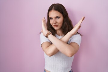 Obraz premium Young hispanic girl standing over pink background rejection expression crossing arms doing negative sign, angry face