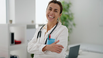 Middle age hispanic woman wearing doctor uniform standing with arms crossed gesture at clinic