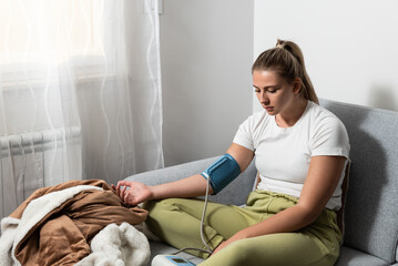 Young sick woman or girl measures her blood pressure with a digital blood pressure monitor. Ill...