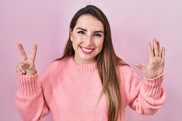 Young hispanic woman standing over pink background showing and pointing up with fingers number seven while smiling confident and happy.