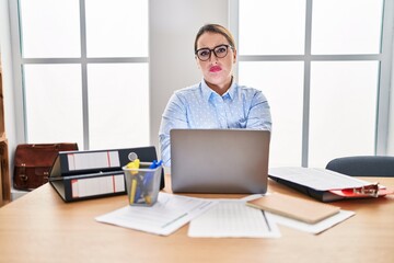 Young hispanic woman working at the office wearing glasses skeptic and nervous, disapproving expression on face with crossed arms. negative person.