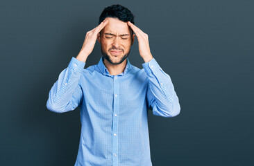 Hispanic man with beard wearing casual business shirt with hand on head for pain in head because stress. suffering migraine.