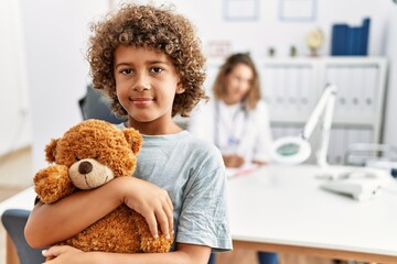 Mother and son smiling confident hugging teddy bear at clinic