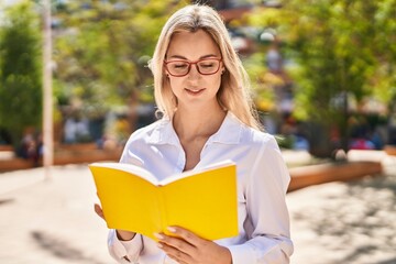 Young blonde woman smiling confident reading book at park