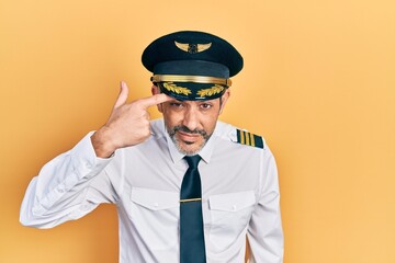 Handsome middle age man with grey hair wearing airplane pilot uniform pointing unhappy to pimple on forehead, ugly infection of blackhead. acne and skin problem