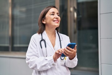 Middle age woman wearing doctor uniform using smartphone at street
