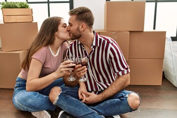 Young caucasian couple kissing and toasting with red wine at new home