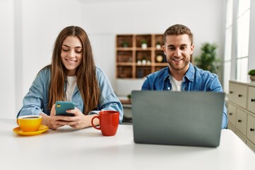 Young caucasian couple having breakfast and using laptop and smartphone at home.