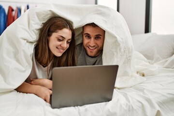 Young hispanic couple watching movie using laptop lying in bed.