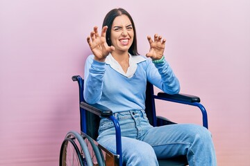 Beautiful woman with blue eyes sitting on wheelchair smiling funny doing claw gesture as cat,...