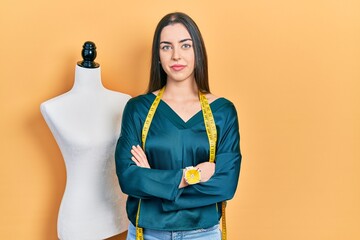 Beautiful woman with blue eyes standing by manikin with crossed arms relaxed with serious expression on face. simple and natural looking at the camera.