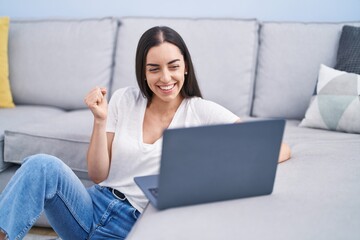 Young brunette woman using laptop at home screaming proud, celebrating victory and success very excited with raised arm