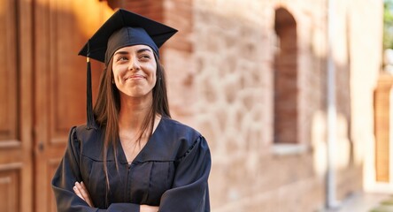Young hispanic woman wearing graduated uniform standing with arms crossed gesture at university