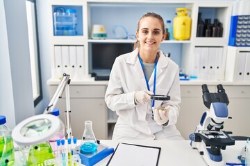 Young blonde woman wearing scientist uniform using loupe at laboratory