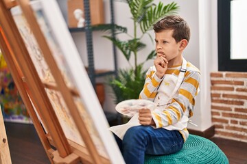 Blond child drawing with doubt expression at art studio