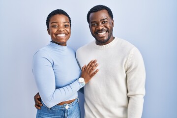 Young african american couple standing over blue background with a happy and cool smile on face....