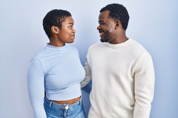 Young african american couple standing over blue background looking to side, relax profile pose...